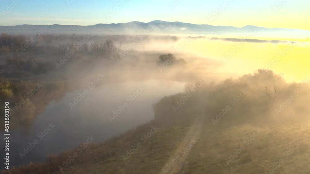 Aerial shot over a river in dense fog during a bright sunrise. Aerial shot over a river in dense fog during a bright sunrise.