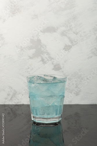 Blue refreshing summer drink. Iced cocktail on grey textured background. Vertical orientation, copy space