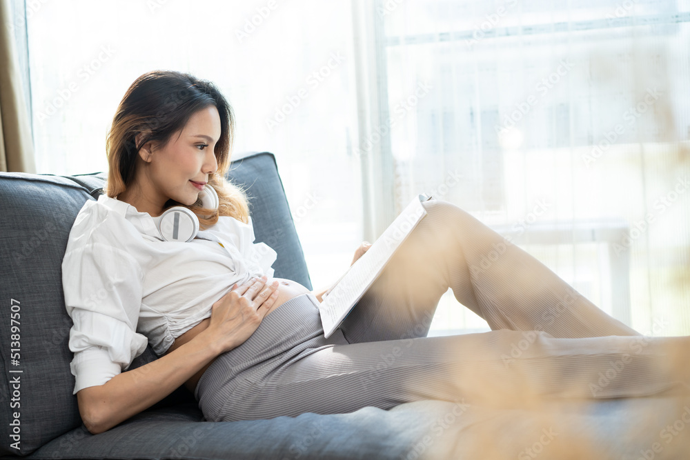Asian young beautiful pregnant woman applying headphones on her belly.