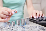 Woman puts coins to a stack of coins and counting on a calculator