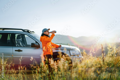 Man drinking coffee by car on mountain