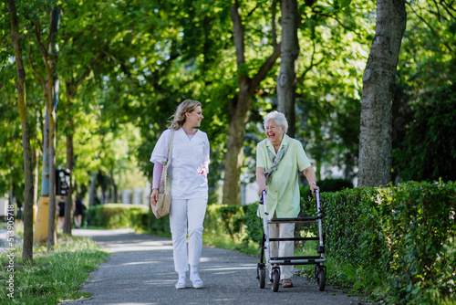 Caregiver with senior woman on walk with walker in park with shopping bag. photo