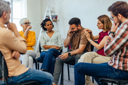 Man holding his tears back, at the group therapy while having support from people around him.