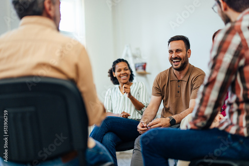An adult man, looking happy, talking with random people from the group therapy.