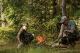 Father with son in military clothes is making campfire in the woods. The concept of adventure, travel, tourism, camping, survival and evacuation.