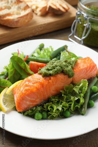 Tasty cooked salmon with pesto sauce served on wooden table, closeup
