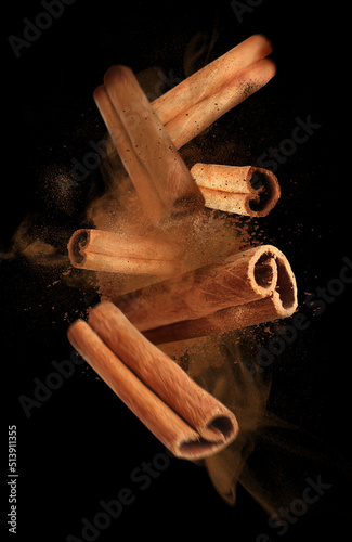 Aromatic cinnamon sticks and powder flying on black background photo