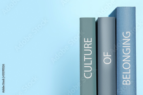 Fotografie Books with phrase Culture of Belonging on light blue background, space for text