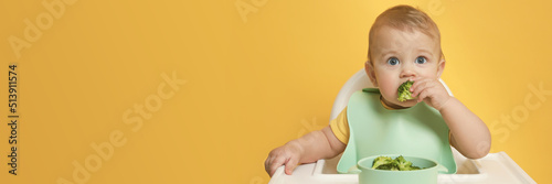 Cute little baby wearing bib while eating on yellow background, space for text. Banner design