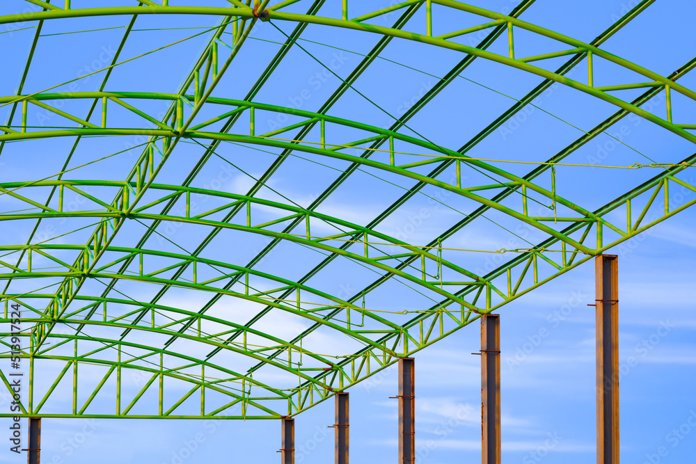Fototapeta premium Low angle view of green metal roof of industrial building structure in construction site against blue sky background