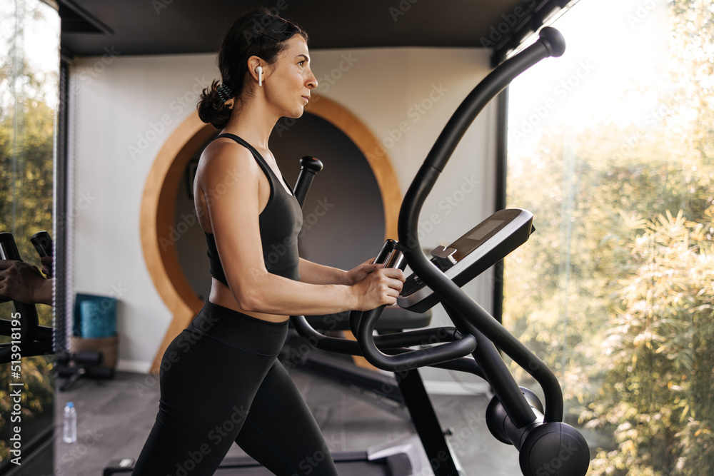 Active caucasian young brunette woman spends time in gym on cardio workout. Girl in sportswear takes care of her body. Healthy lifestyle concept. Active caucasian young brunette woman spends time in gym on cardio workout. Girl in sportswear takes care of her body. Healthy lifestyle concept.