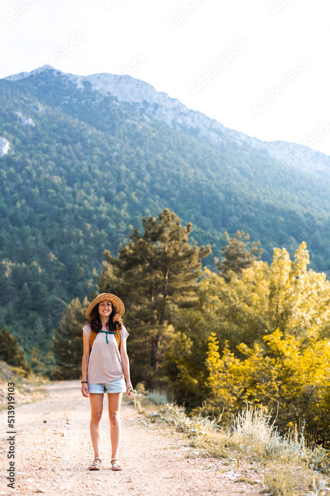A girl with a backpack and a straw hat walks along a mountain path