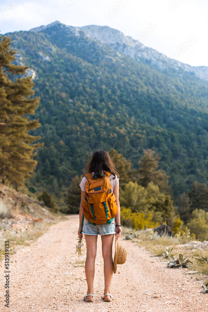 A girl with a backpack and a straw hat walks along a mountain path