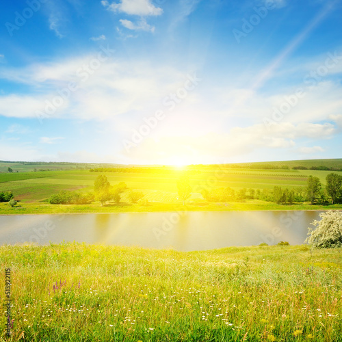 Meadow, lake, agricultural fields and sunrise on blue sky.