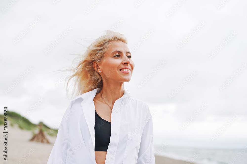 Portrait of Elegant blonde woman in white shirt on sand beach at storm sea Portrait of Elegant blonde woman in white shirt on sand beach at storm sea