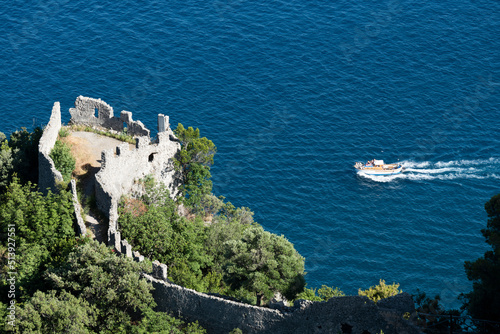 Obraz na płótnie View from above, stunning view of a gozzo boat with tourists on board sailing on a blue water. Defocused Torre dello Ziro in the foreground. Amalfi Coast, Italy. w salonie