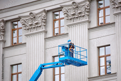 Fotografiet Construction worker in lift bucket of crane restore and repair historic facade of building