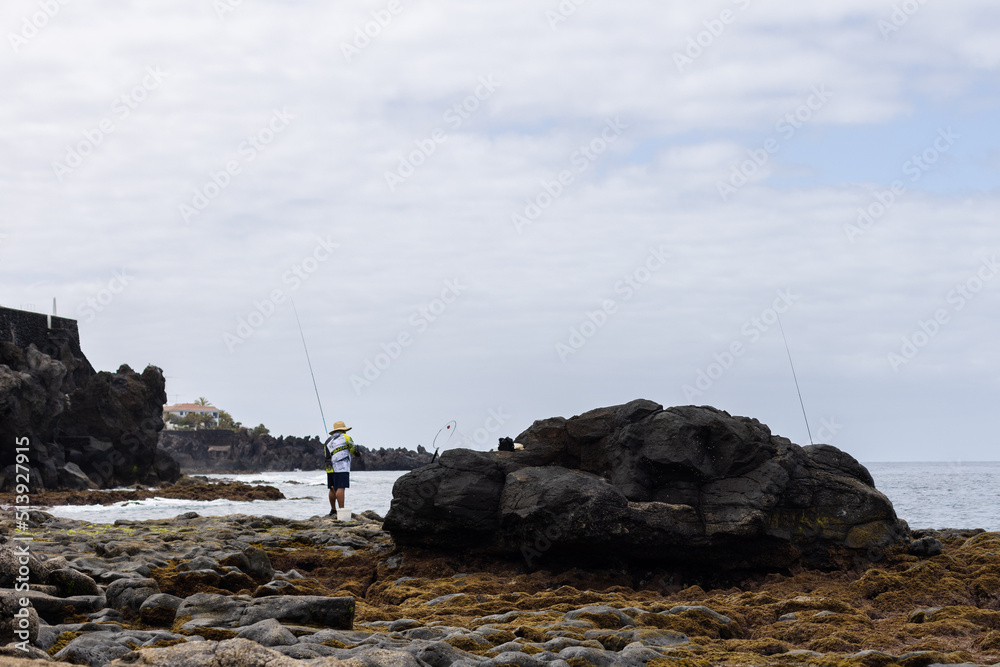 Fototapeta premium Unrecognisable fisherman in the morning. Volcanic rocky beach.