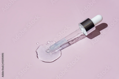 Transparent pipette with blue cosmetics serum on a light pink background. Product texture. Dropper glass bottle branding mockup. Cosmetic pipette.