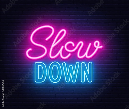 Slow Down neon lettering on brick wall background.