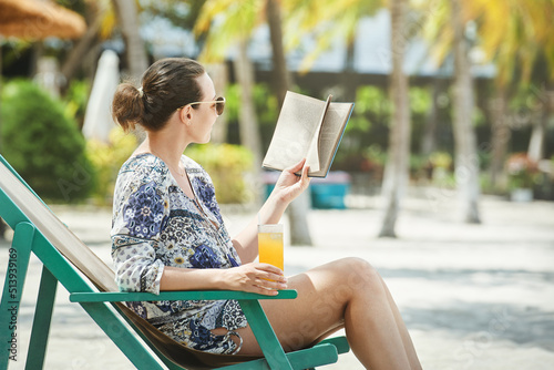 Print op canvas Happy smiling woman sitting in deck chair reading book at beach  in resort