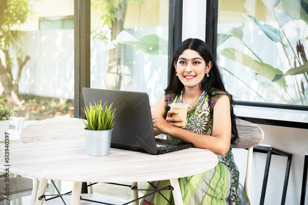 Indian woman with laptop on the table holding coffee Indian woman with laptop on the table holding coffee