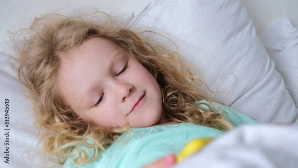 Caucasian curly cute preschool kid girl smile using smartphone technology device lying on bed alone. Small child hold smartphone surfing internet play game at home. Children tech addiction Caucasian curly cute preschool kid girl smile using smartphone technology device lying on bed alone. Small child hold smartphone surfing internet play game at home. Children tech addiction