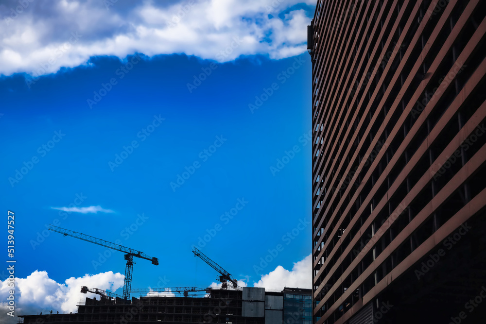 Construction cranes work on creation site against sky background