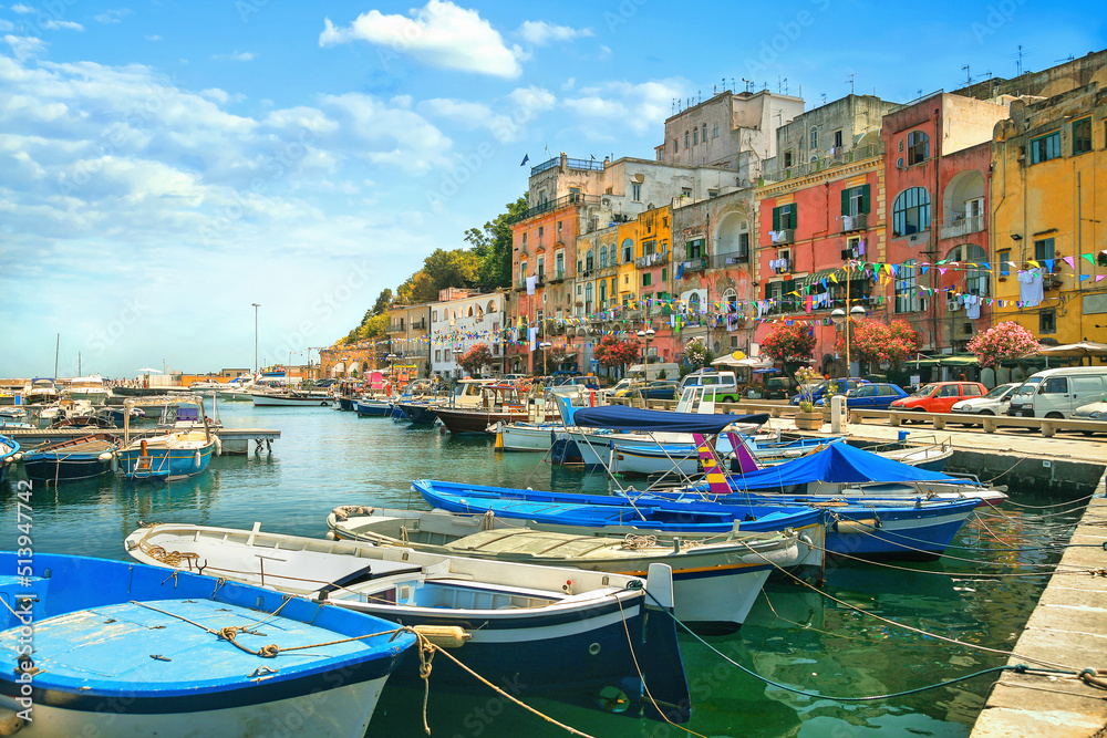 Main street with colorful houses and marina with fishing boats in Procida old town. Italy