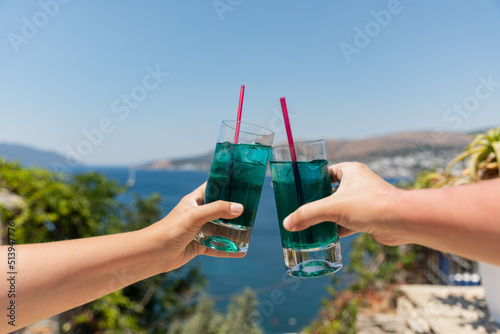 Cheers! Couple toasting with tropical chilled blue drinks with ice at hot sunny day. Summer soft drinks.