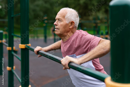 Sportive elderly man doing street fitness on the simulator in park