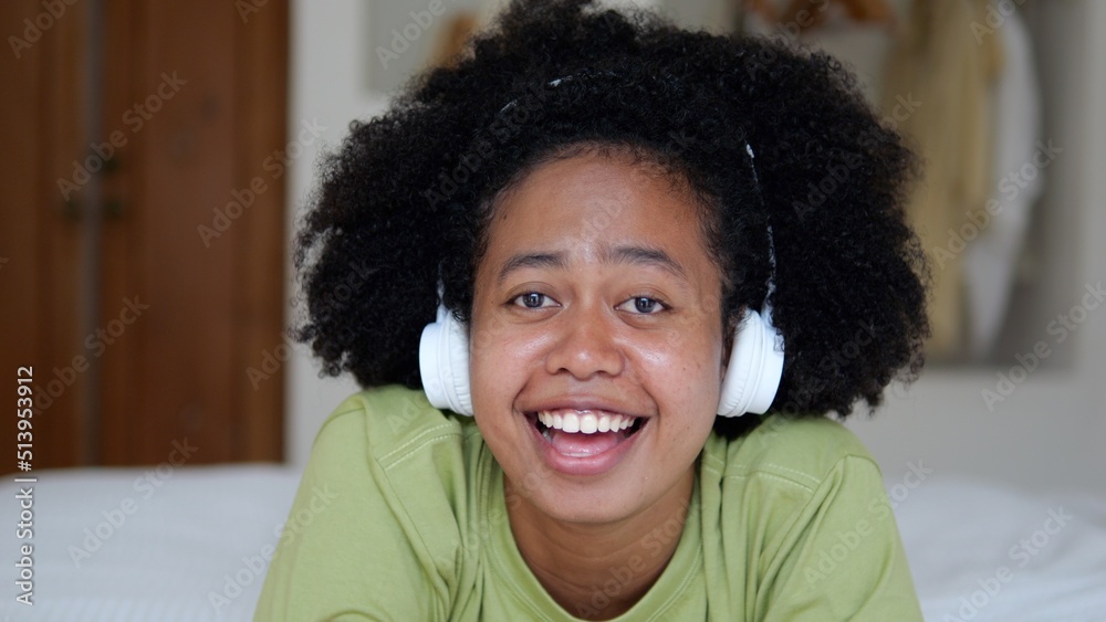 A singing woman lies on a bed in a room, listens to music on headphones and sings along with a smile. Mixing races of Africans and Asians in America. The carefree life of a young woman. A singing woman lies on a bed in a room, listens to music on headphones and sings along with a smile. Mixing races of Africans and Asians in America. The carefree life of a young woman.