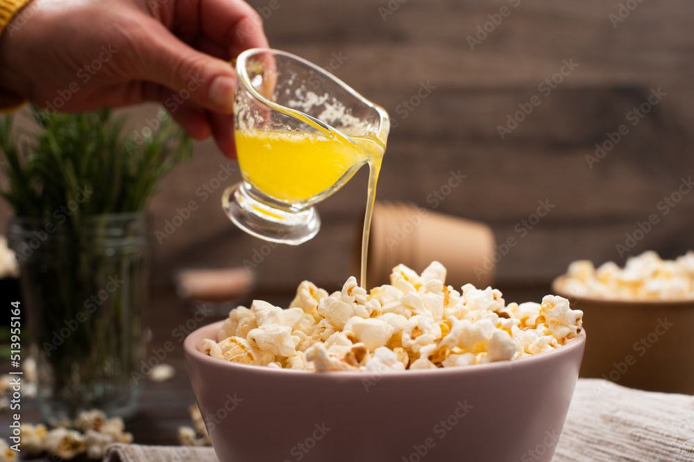 Melted butter being poured on popcorn in clay bowl on kitchen table