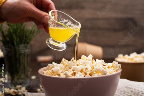 Melted butter being poured on popcorn in clay bowl on kitchen table