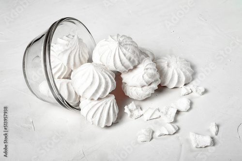 glass vase with a French dessert meringue lies on a gray background, part of the meringue has spilled out of the vase onto the table. whole and broken parts of the meringue are visible. side view.