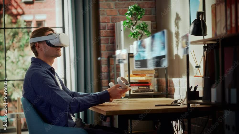 Excited Young Man Sitting in Loft Living Room at Home, Using Virtual Reality Headset with Controllers to Check Social Media Streaming Application. Male Choosing to Watch American Football Highlights. Excited Young Man Sitting in Loft Living Room at Home, Using Virtual Reality Headset with Controllers to Check Social Media Streaming Application. Male Choosing to Watch American Football Highlights.