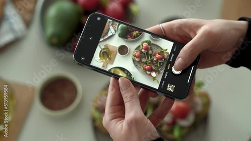 Closeup of female hands holding smartphone and taking pictures for social media in kitchen, cooking dietary meal from fresh vegetables and toasts. healthy eating concept. Vertical shoot. 4k footage