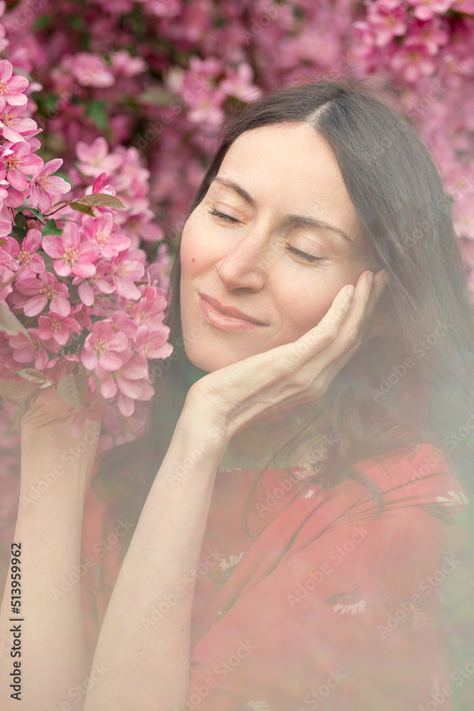 Young pretty woman enjoys standing near a blooming spring tree. A girl in a red dress smiles among the blooming apple trees. The concept of the spring season. Young pretty woman enjoys standing near a blooming spring tree. A girl in a red dress smiles among the blooming apple trees. The concept of the spring season.