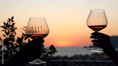 Close-up view of silhouette of wine glasses clinking during a dinner against the background of a beautiful sunset. Cute couple celebrate their anniversary. Romantic dating concept. 4k footage
