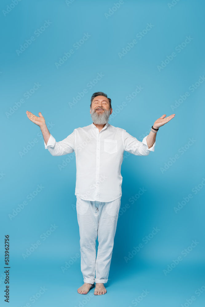 barefoot bearded man with closed eyes meditating in tree pose with open arms on blue. barefoot bearded man with closed eyes meditating in tree pose with open arms on blue.