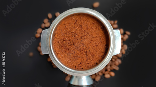 Amped puck of coffee grounds within basket of portafilter and coffee beans spilled around in a dark and moody scene of natural light.