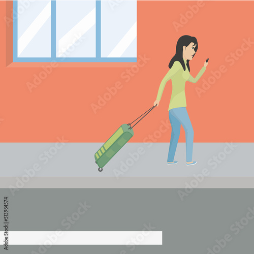 woman carrying her suitcase on the sidewalk is looking at her phone.
