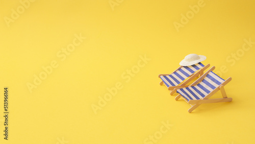 Two blue white stripe deck chairs with straw hat on yellow .paper background. Tropical copy space. Summer travel vacation concept. Minimal composition. Vacation for couples. Valentine travel.