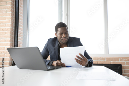 portrait of stylish african man in suit at table with laptop