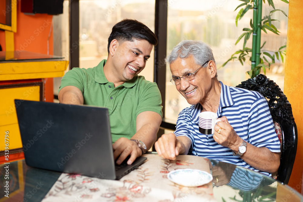 Young indian son and old father using laptop together. Younger generation teaching senior people how to use computer. Asian Family using internet or web surfing at home. Young indian son and old father using laptop together. Younger generation teaching senior people how to use computer. Asian Family using internet or web surfing at home.