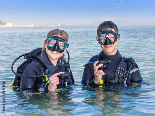 Smiling scuba divers in the sea, facing the camera with their dive masks on and their regulators in their hands