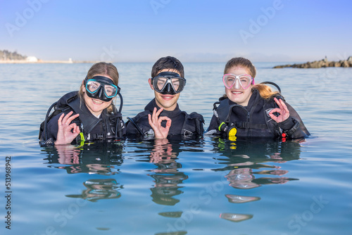 Smiling scuba divers in the sea, facing the camera with their dive masks on showing the OK sign