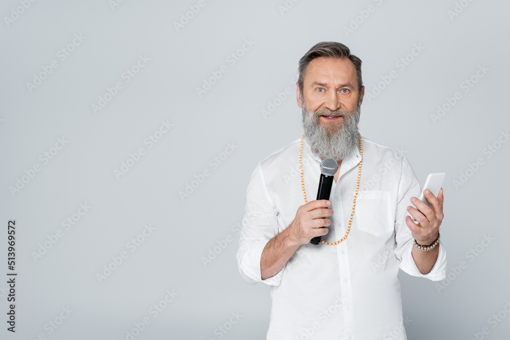motivational guru with mobile phone talking in microphone isolated on grey. motivational guru with mobile phone talking in microphone isolated on grey.