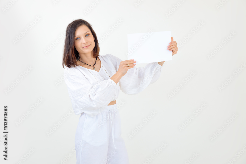 Attractive, pretty smiling and confident brunette woman in white outfit hold paper on white background, look at camera Attractive, pretty smiling and confident brunette woman in white outfit hold paper on white background, look at camera