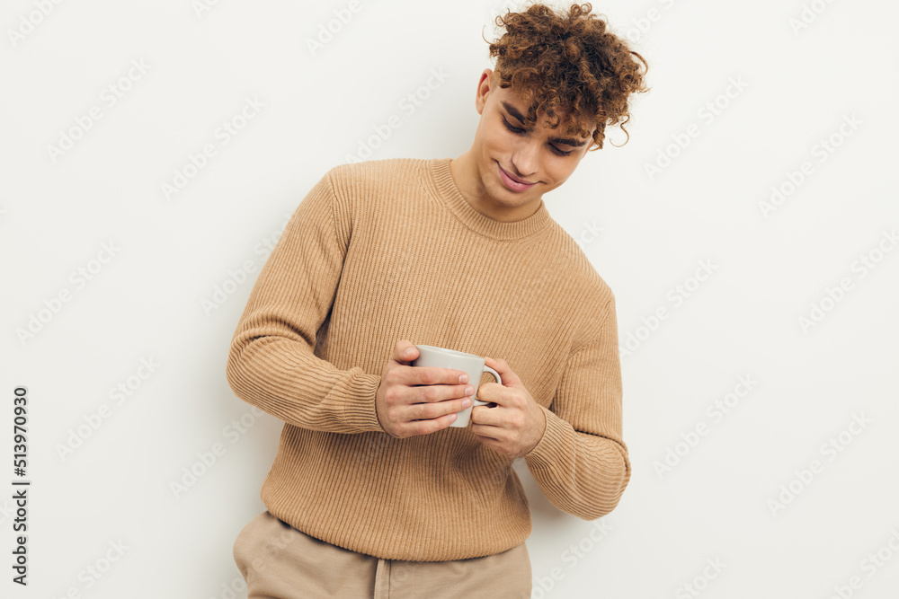 a cute, stylish man stands on a light background holding a white cup in his hand and looks down a cute, stylish man stands on a light background holding a white cup in his hand and looks down
